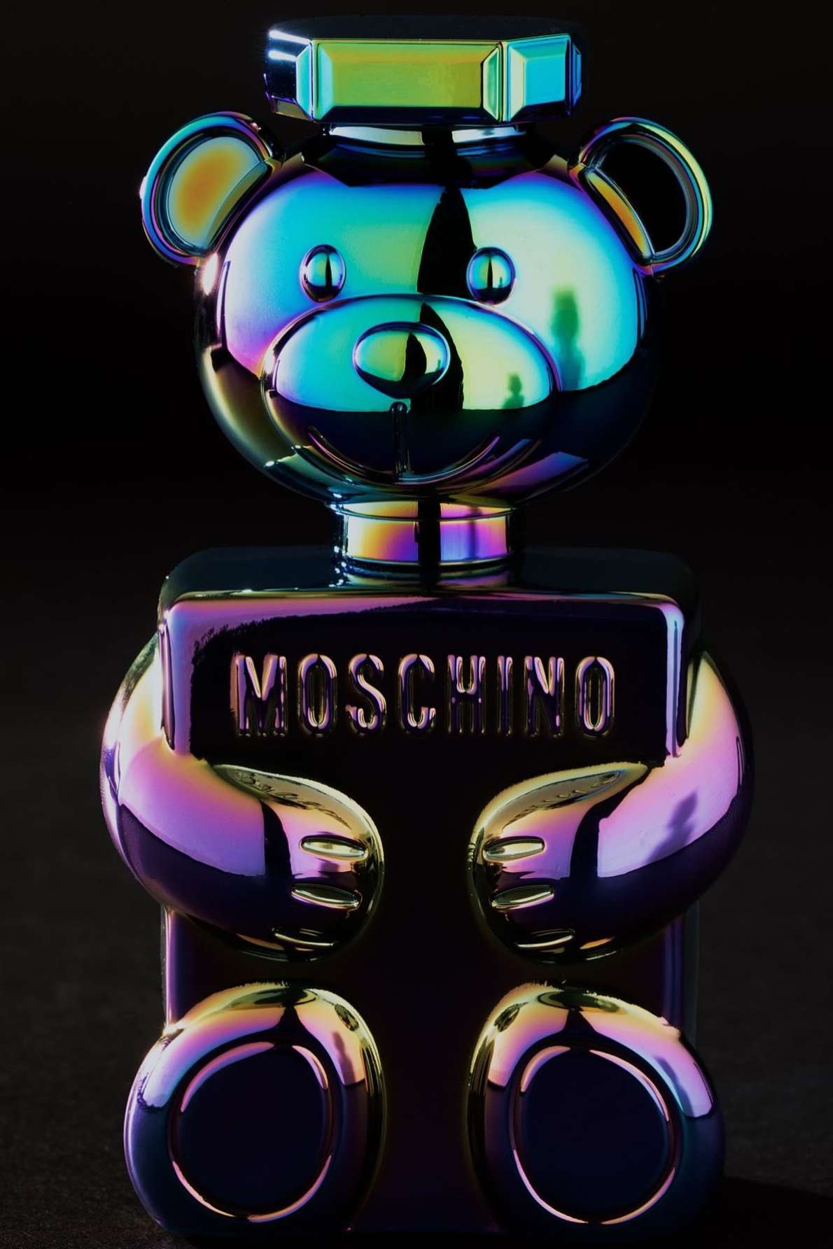 Moschino Toy 2 Bubble Gum perfume bottle, shaped like a teddy bear, features an iridescent color scheme on a dark background.