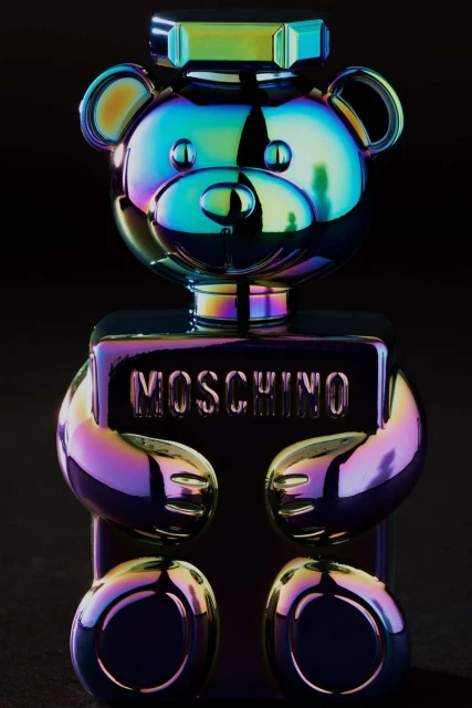Moschino Toy 2 Bubble Gum perfume bottle, shaped like a teddy bear, features an iridescent color scheme on a dark background.