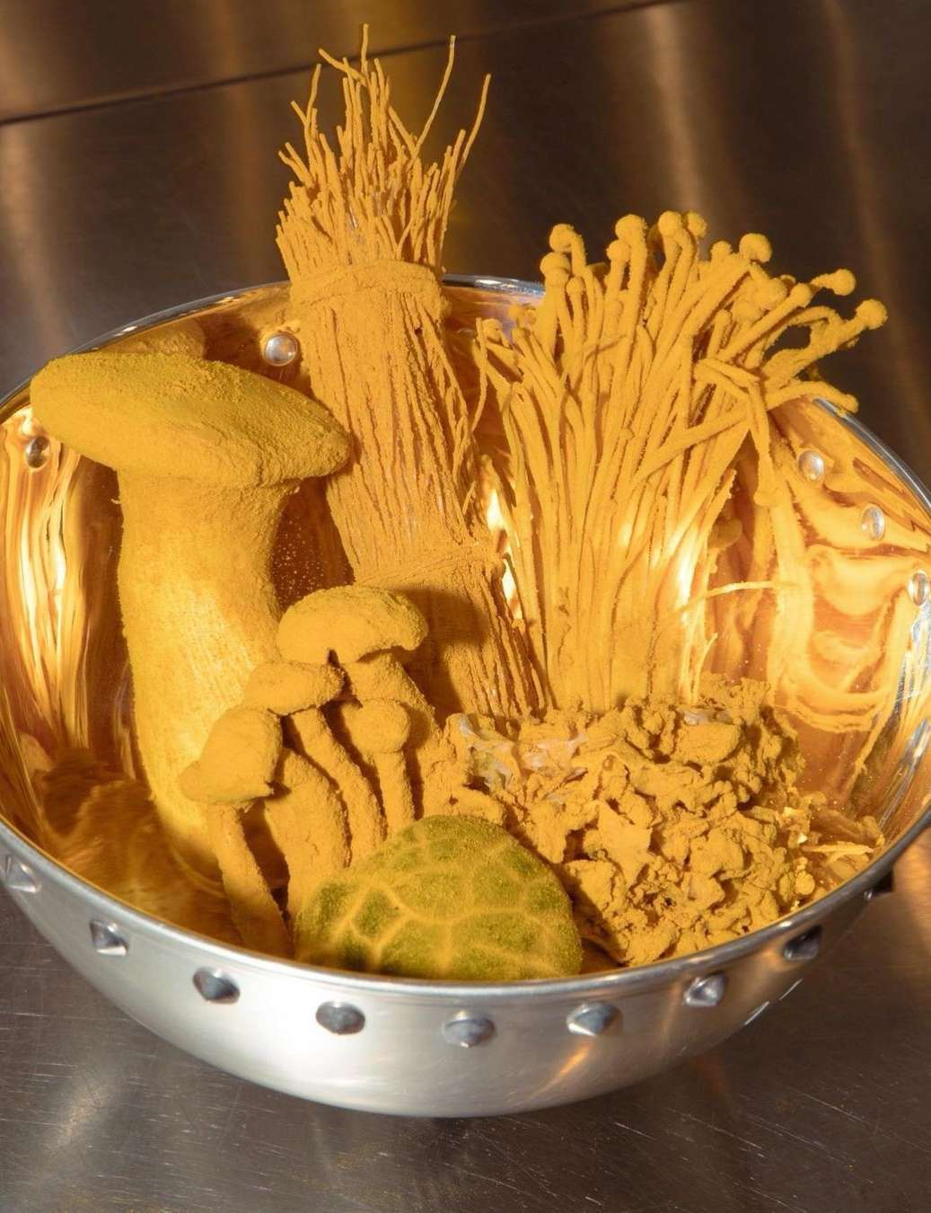 A bowl contains several types of golden-yellow mushrooms: enoki, and a larger capped variety, dusted with a powdery substance.
