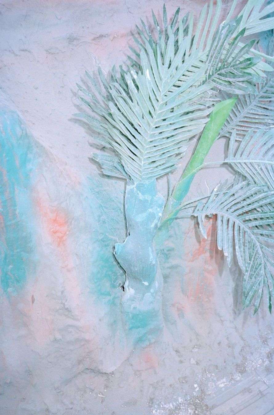 Stylized palm tree and sand dune-like background in cool shades of blue, white, and orange, evokes a surreal beach scene.