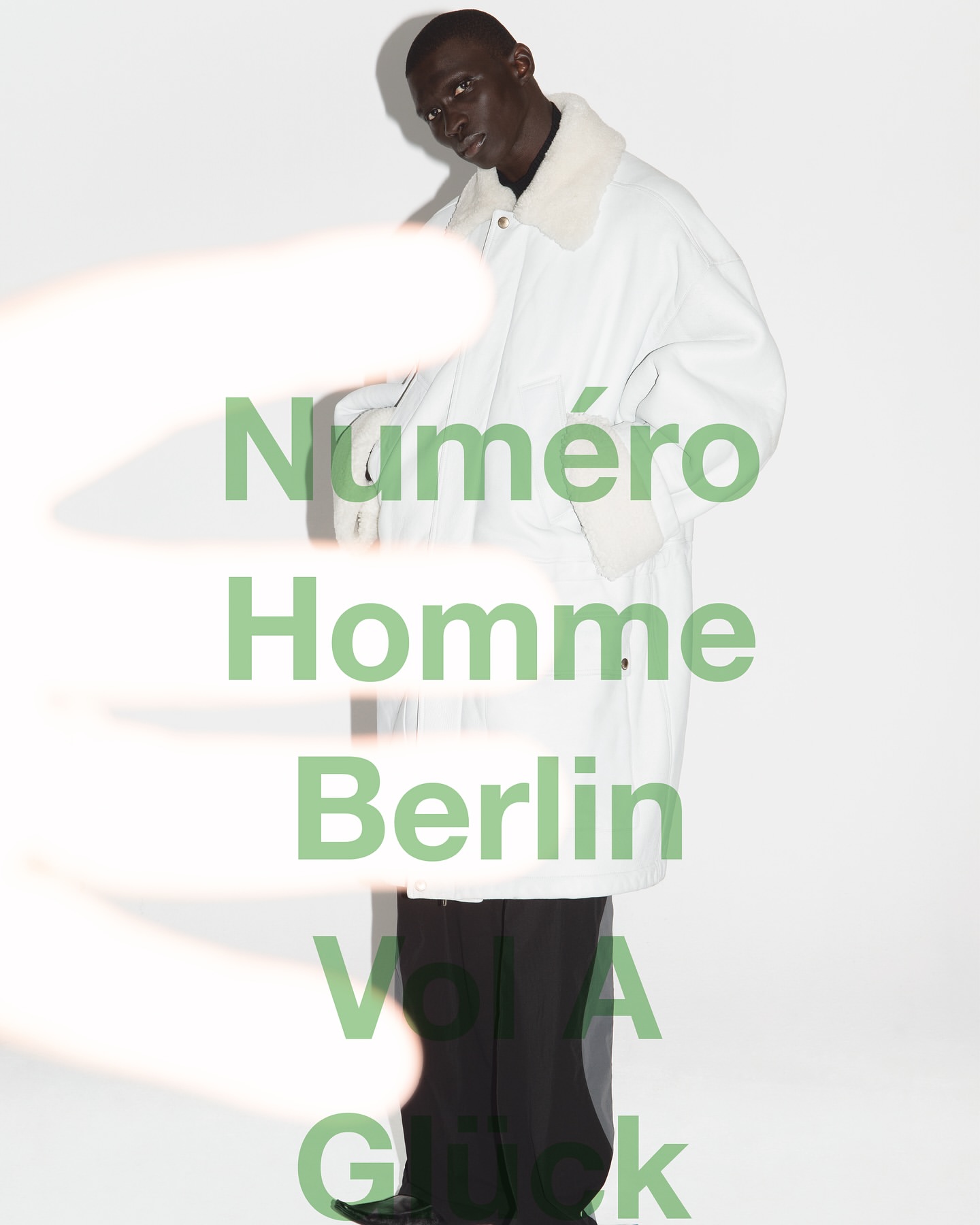 Editorial fashion portrait of an African-American male model in a white coat, posing against a white background with bold text overlay.