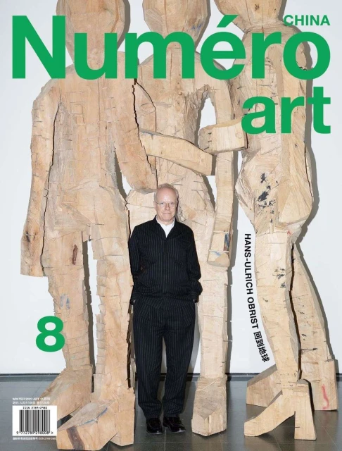 Numero Art China magazine cover featuring Hans-Ulrich Obrist standing in front of three wooden figures, in front of a white wall.