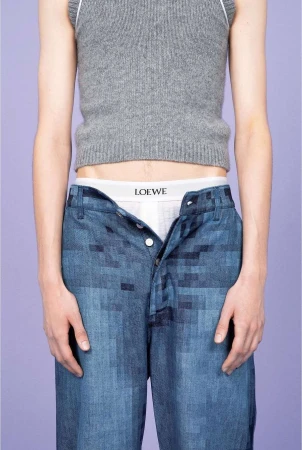 Fashion shot featuring a slender adult in a grey top and blue patterned pants, revealing white underwear against a light purple backdrop.