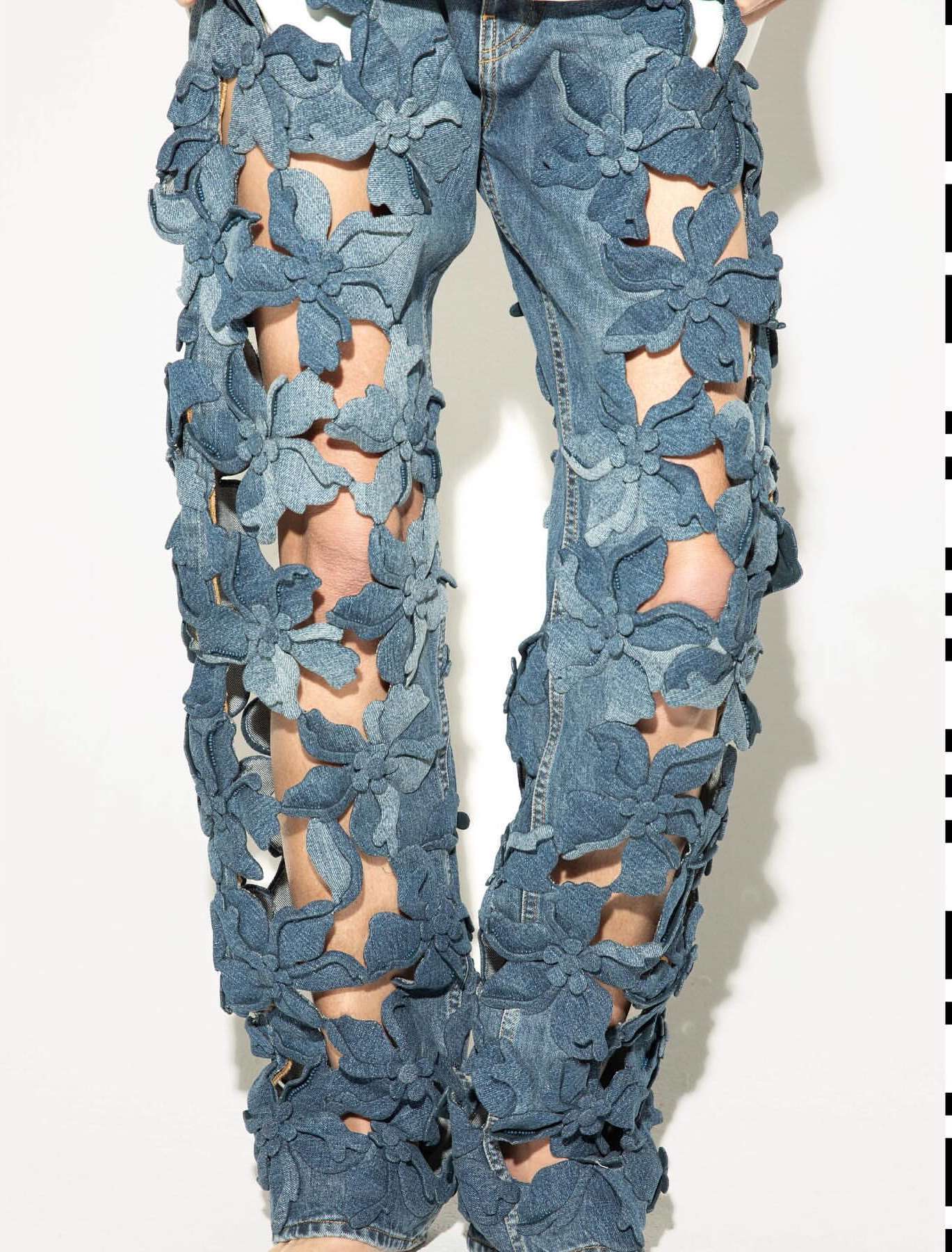 Denim pants with floral cutouts worn in front of a white background. Creative blue jeans are a modern and unique fashion statement.