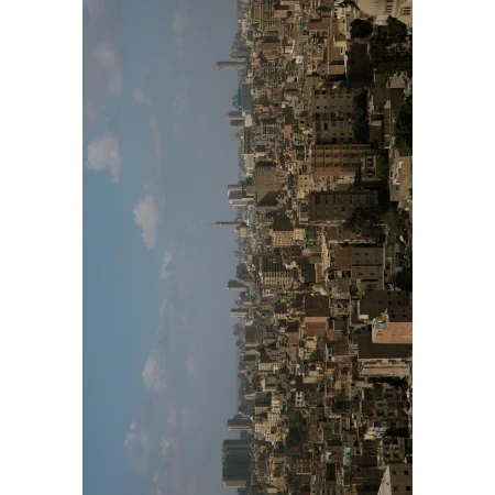 Cityscape aerial view featuring dense buildings, a tall tower, and a hazy blue sky with scattered clouds, showcasing urban architecture.
