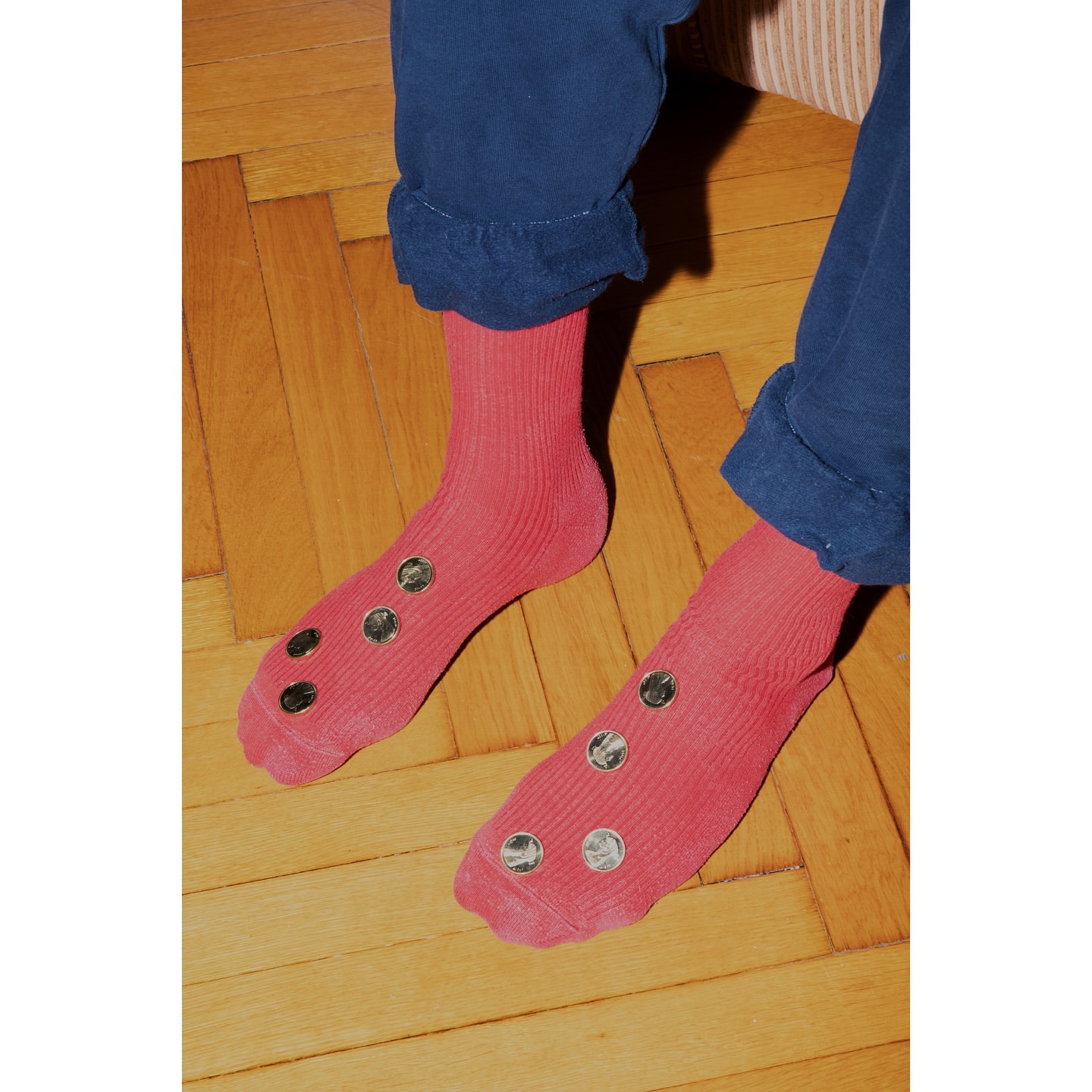 Close-up shot of two legs wearing pink socks decorated with round, silver embellishments, set against a wooden floor background.