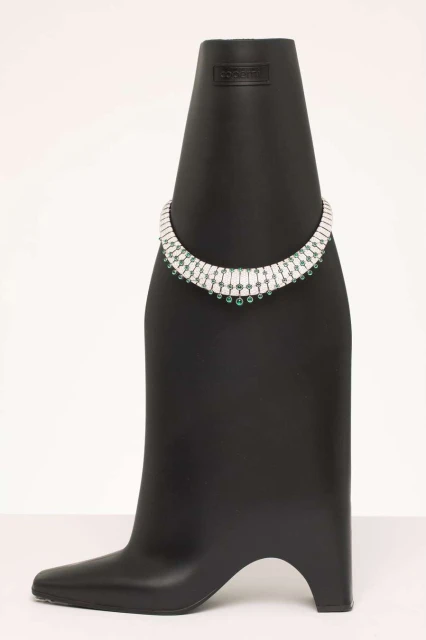 Necklace with green stones and diamonds on a black display bust against a white background in a studio setting. Jewelry concept.