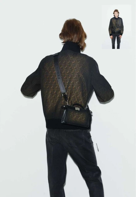 Male fashion model poses in patterned jacket and dark jeans with Fendi purse and crossbody strap against a white background.
