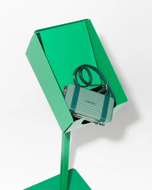 RIMOWA handbag on a green metal display stand against a white backdrop in a studio setting, showcasing luxury fashion and design.
