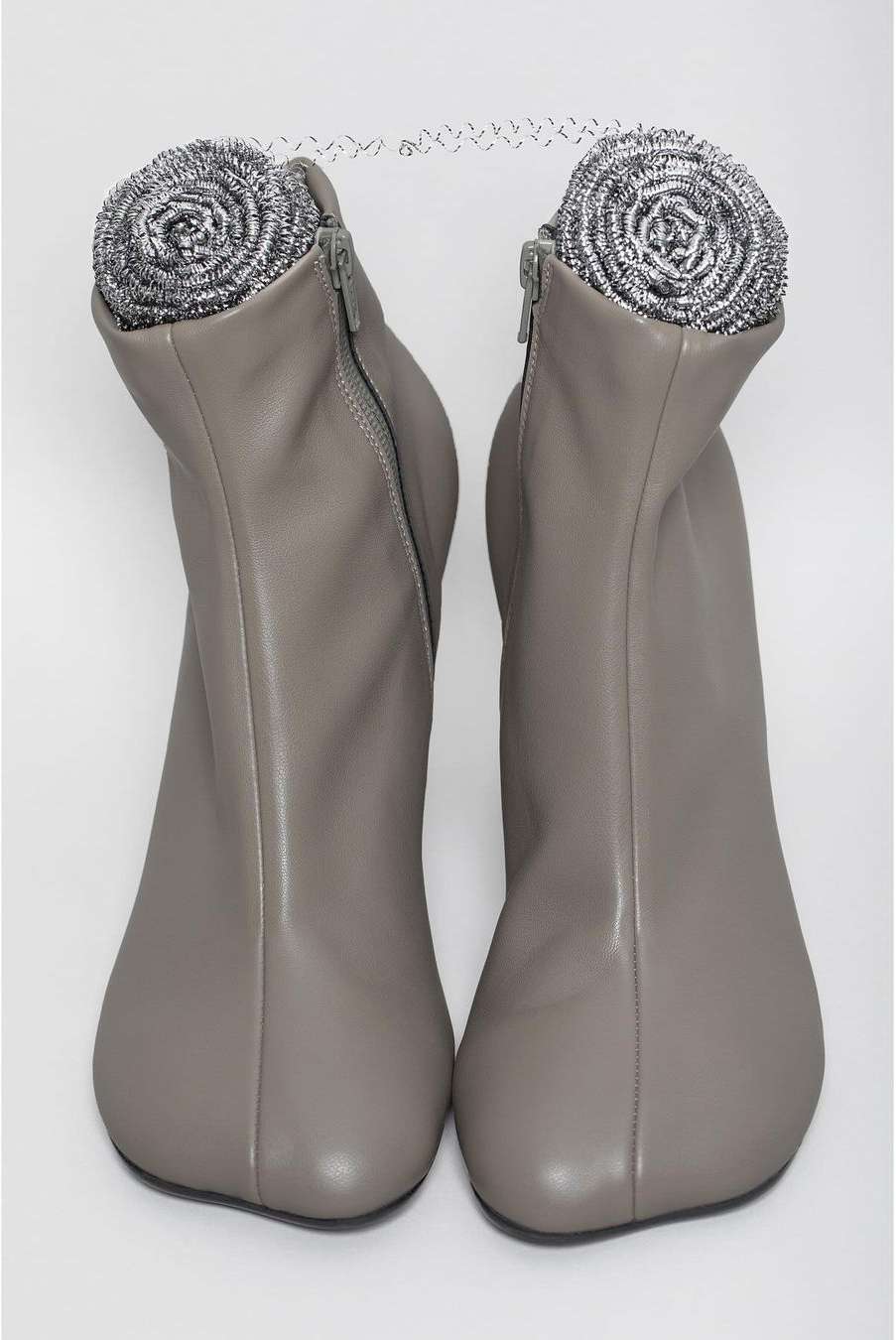 Two grey ankle boots are displayed side by side against a white backdrop, with a stainless steel scouring pad placed inside each boot.