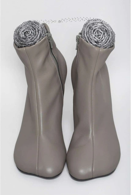 Two grey ankle boots are displayed side by side against a white backdrop, with a stainless steel scouring pad placed inside each boot.