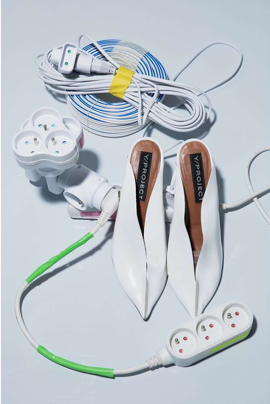 White heeled mules with power strips and extension cords, studio shot against a plain background. Fashion and technology theme.
