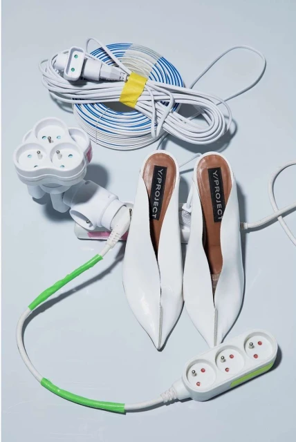 White heeled mules with power strips and extension cords, studio shot against a plain background. Fashion and technology theme.