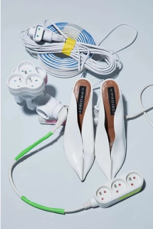 White heeled mules with power strips and extension cords, studio shot against a plain background. Fashion and technology theme.
