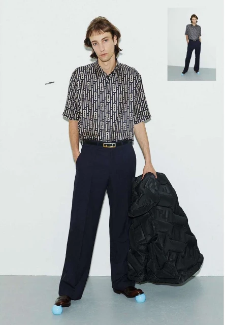 Man in patterned shirt and dress pants posing with black jacket against white backdrop. Full shot of fashion look, studio lighting.