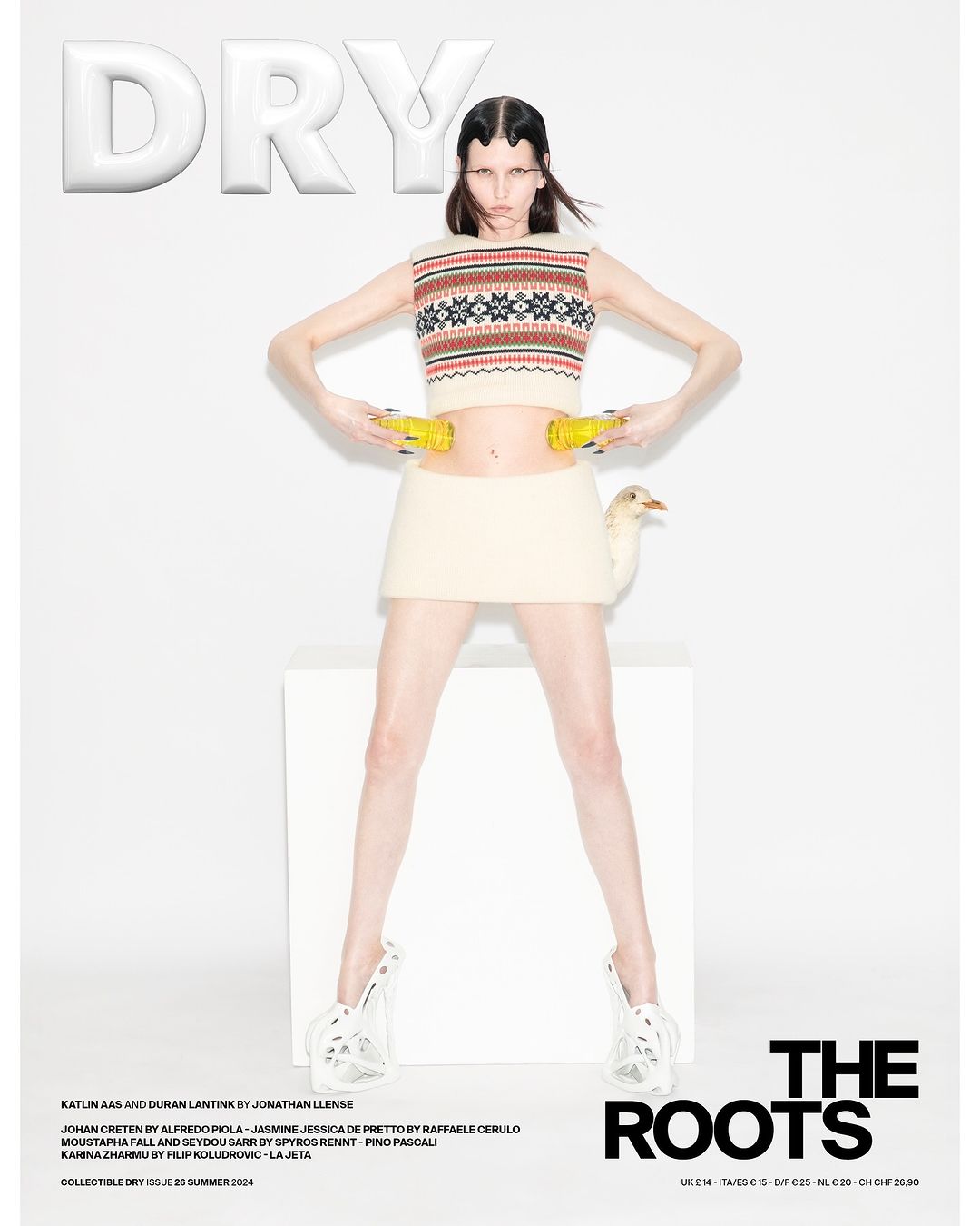 Editorial fashion shot of a young female adult posing in a cropped sweater and skirt with yellow objects, white background and cube.