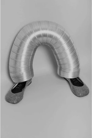 Eye-level shot featuring a pair of ballet flats with a person partially visible under a corrugated metal pipe in a grey studio.