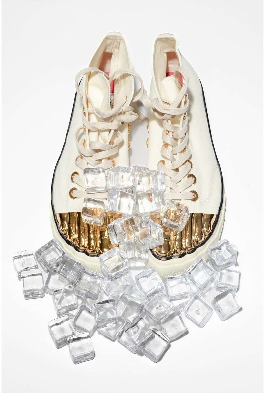 High-top sneakers with laces, set against a white backdrop, partially covered by a collection of clear, artificial ice cubes.