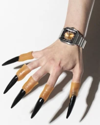 Close-up of a human hand wearing a silver watch and prosthetic claw fingernails against a white background.