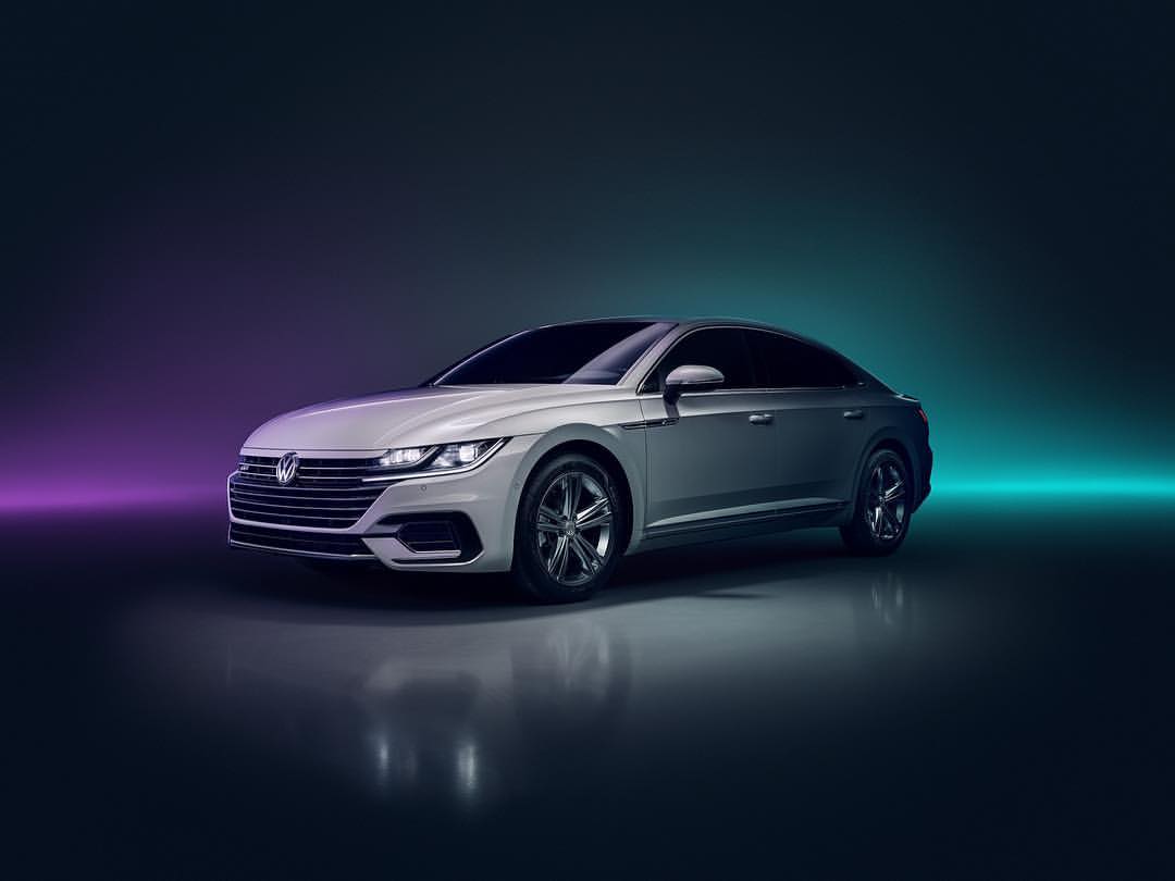 Silver Volkswagen Arteon sedan in a studio setting with dramatic teal and purple lighting, showcasing automotive design.
