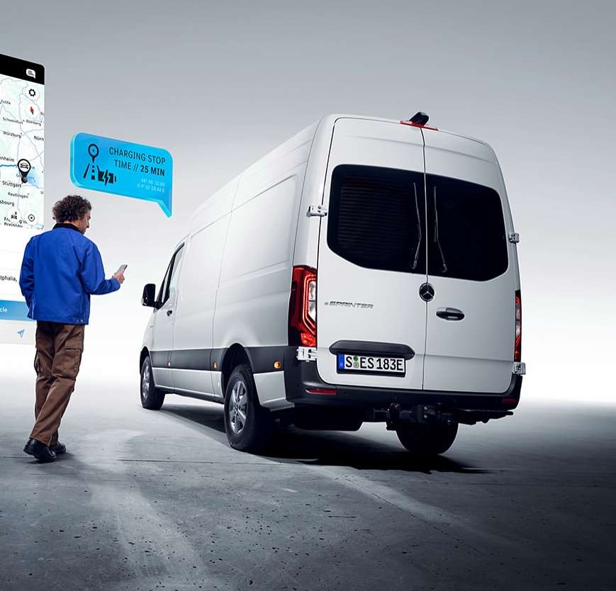 eSprinter van parked with a man using a smartphone and an app showing nearby charging stations with a charging stop time of 25 minutes.