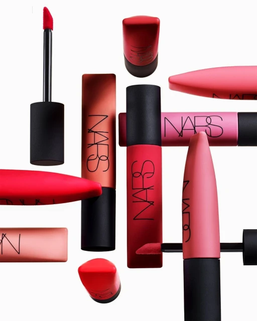 Still life arrangement of NARS brand lipsticks in various shades of red and pink against a white background, product photography.