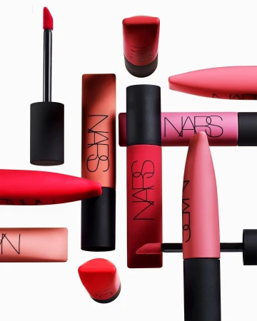 Still life arrangement of NARS brand lipsticks in various shades of red and pink against a white background, product photography.