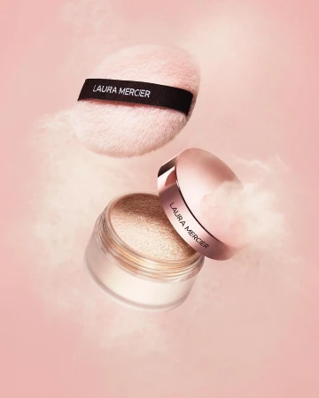 Laura Mercier powder and puff on pink background. Powder floats around the makeup products in a beauty product promotional shot.