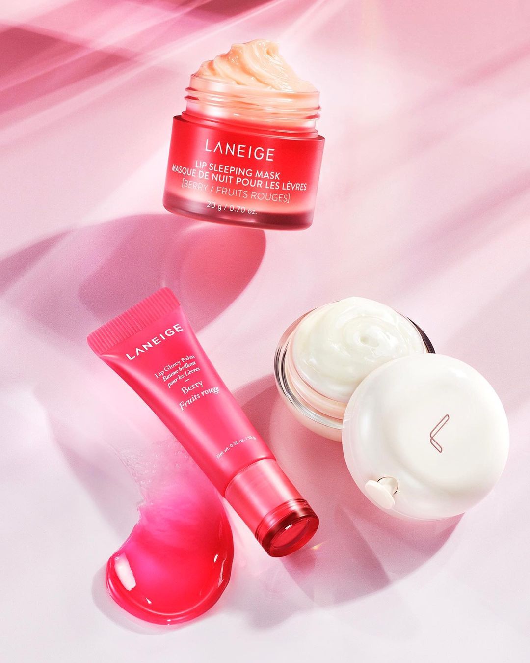 Close-up studio shot of Laneige lip care products, including lip sleeping mask and lip glowy balm, with pink lighting and soft shadows.