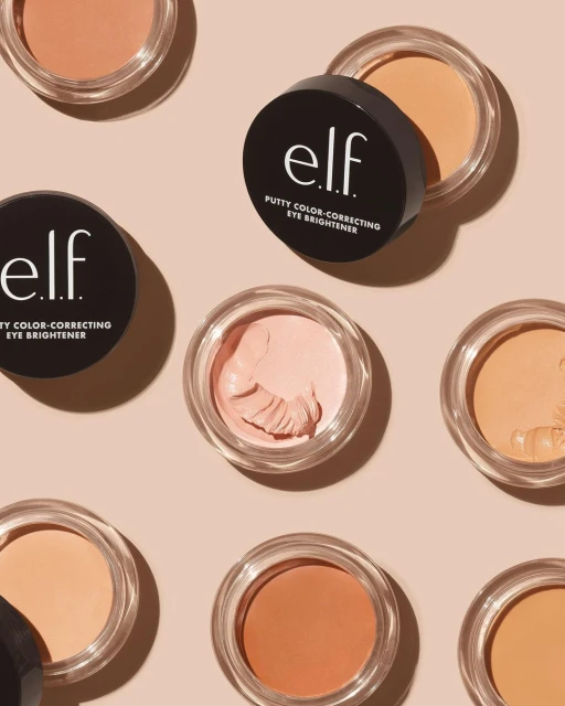 Eye brightener product display with several containers of ELF putty color-correcting cream arranged on a light pink background.