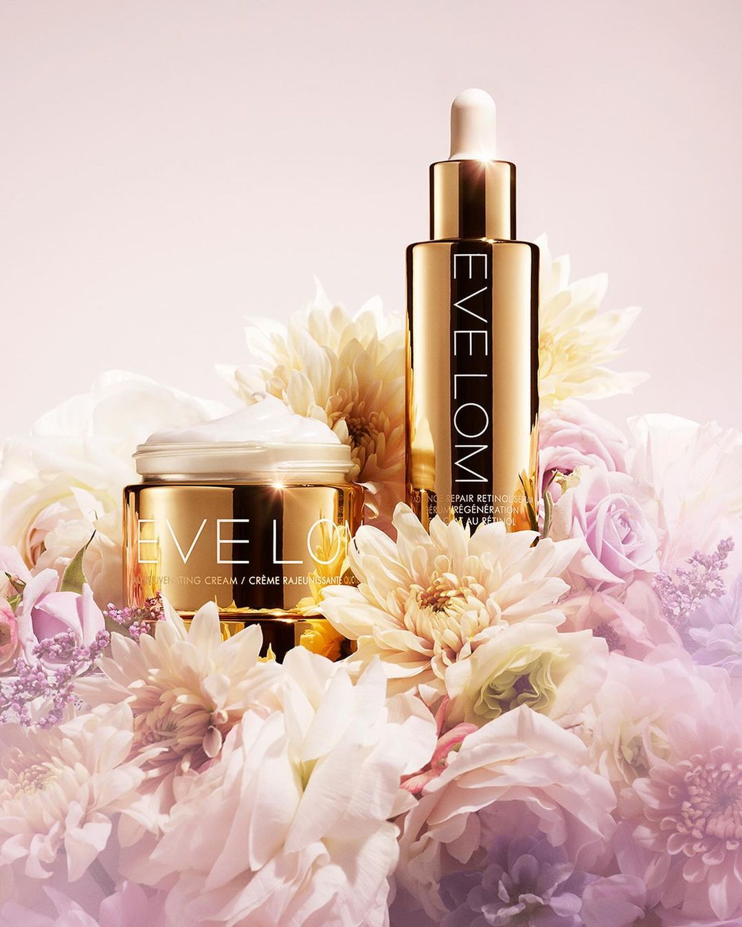 Product shot of Eve Lom skincare products. Retinol elixir and moisturizing cream, featuring gold packaging and white flowers.