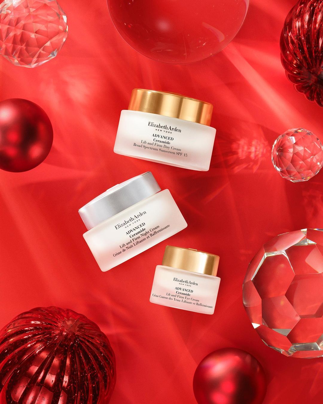 Three Elizabeth Arden skincare cream jars on a red background, accented with red and clear decorative orbs. Beauty product flat lay.