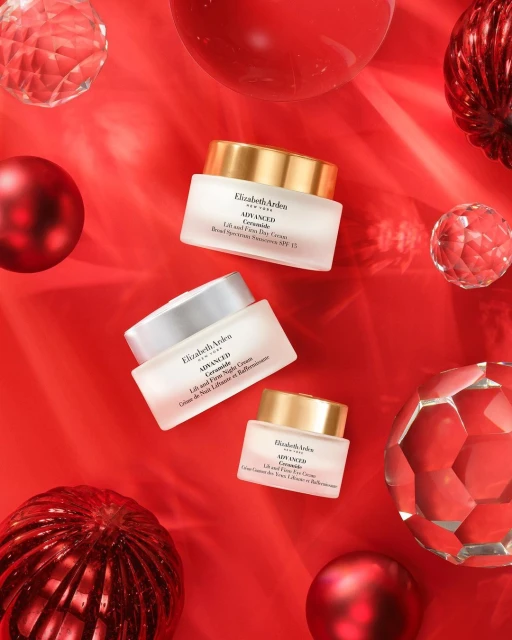 Three Elizabeth Arden skincare cream jars on a red background, accented with red and clear decorative orbs. Beauty product flat lay.