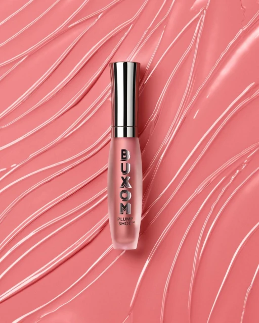 Buxom Plump Shot lip gloss product shot on a peach-colored surface with abstract lines and smears creating a visually dynamic beauty image.