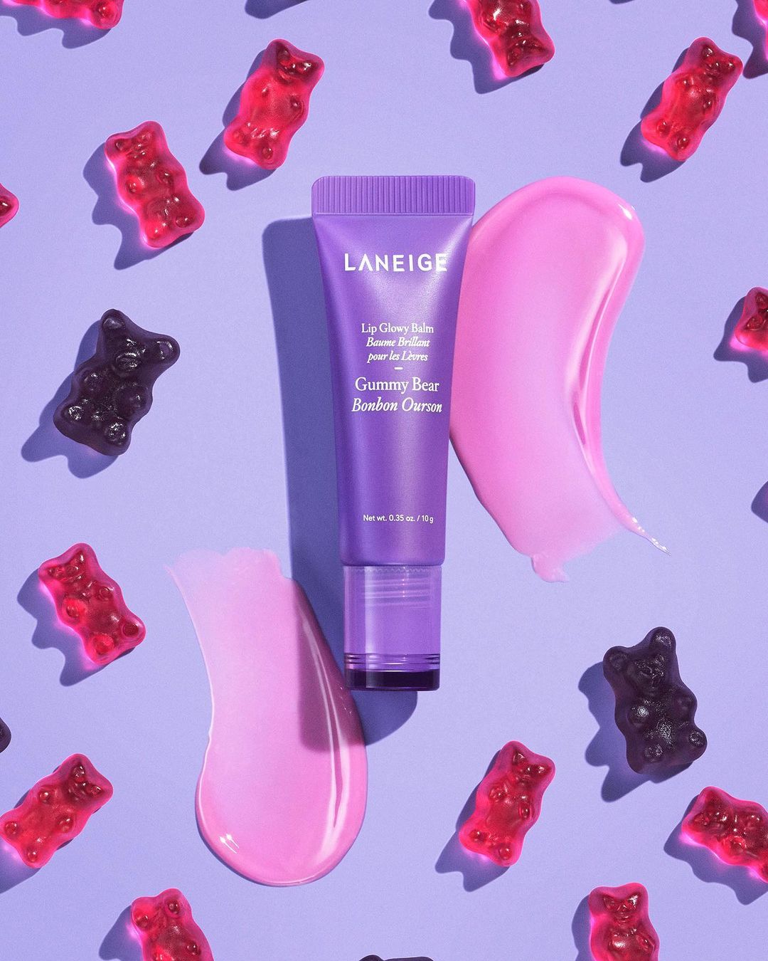 Laneige lip balm tube with pink lip balm swatch and gummy bears on a light purple background. Beauty product flat lay.
