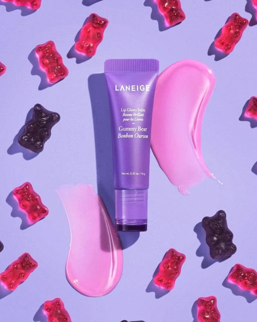 Laneige lip balm tube with pink lip balm swatch and gummy bears on a light purple background. Beauty product flat lay.