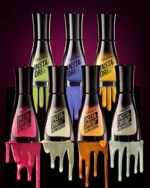 Multiple bottles of Sally Hansen Insta-Dri Glow in the Dark nail polish in various colors and finishes displayed on a black background.