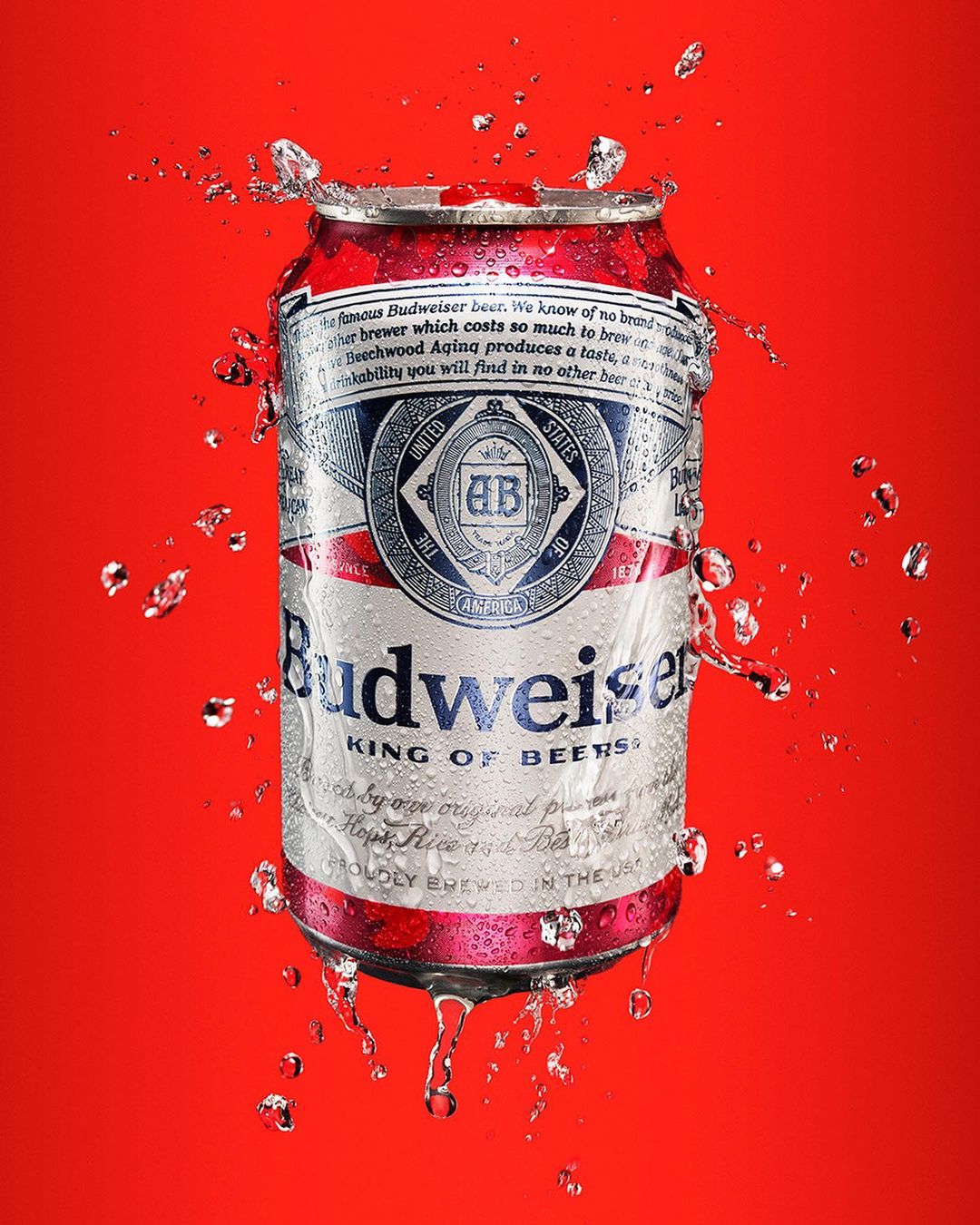 A Budweiser beer can surrounded by water droplets against a vibrant red background, showcasing a refreshing and visually appealing beverage shot.