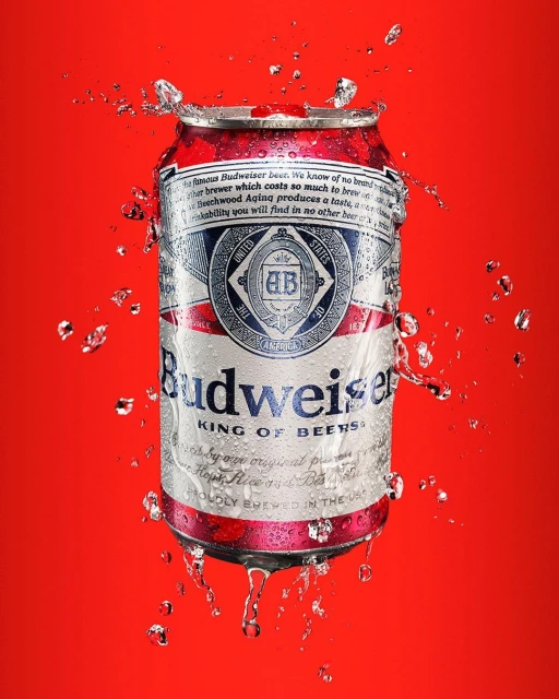 A Budweiser beer can surrounded by water droplets against a vibrant red background, showcasing a refreshing and visually appealing beverage shot.