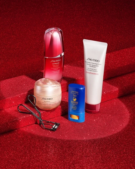 Cosmetic still life of Shiseido skincare products against a red glitter background, including cleanser, serum, cream, and sunscreen.