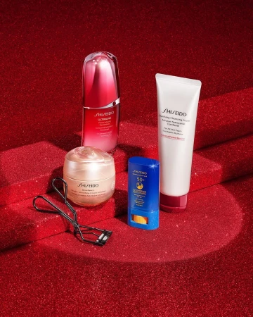 Cosmetic still life of Shiseido skincare products against a red glitter background, including cleanser, serum, cream, and sunscreen.