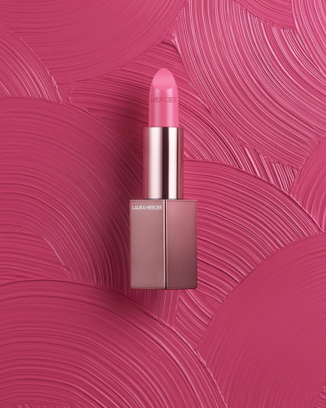Close-up of a pink Laura Mercier lipstick against a matching pink textured surface, product photography, beauty, cosmetic product.