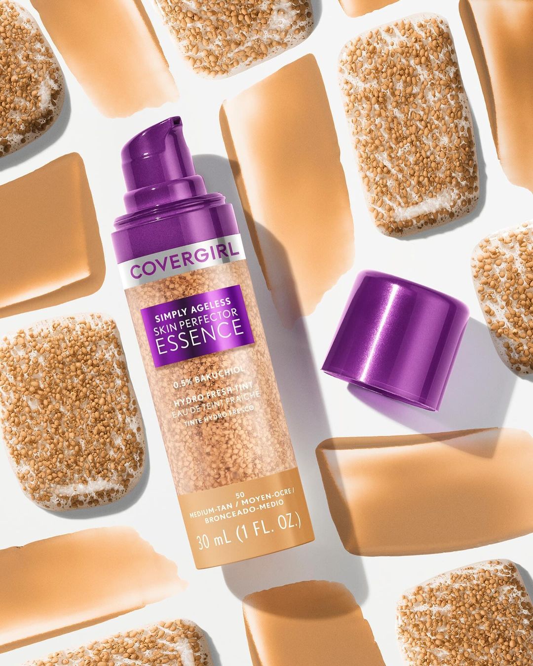 CoverGirl Simply Ageless Skin Perfector Essence foundation bottle with open lid, surrounded by swatches of foundation and small sponges.