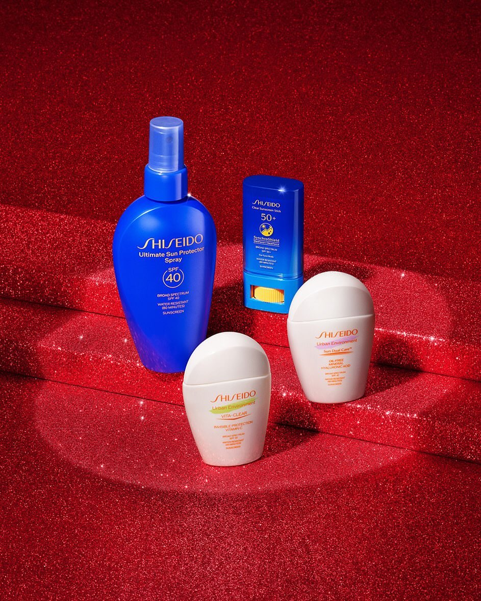 Assortment of Shiseido sun protection products including sprays and creams against a red glittery background in a beauty shot.