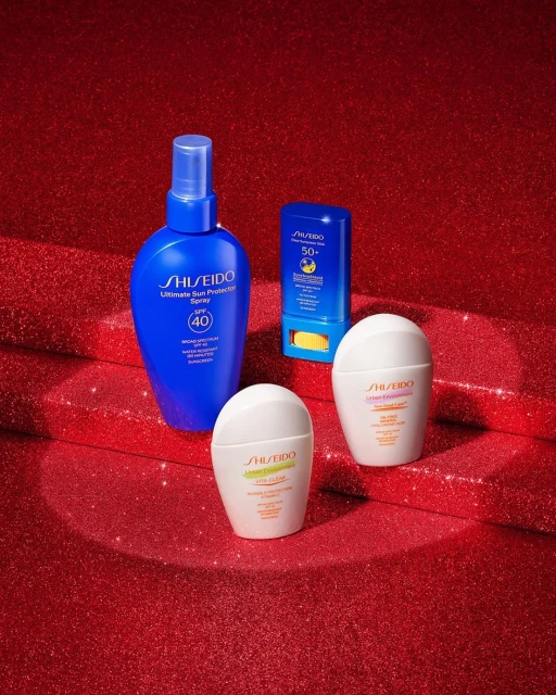 Assortment of Shiseido sun protection products including sprays and creams against a red glittery background in a beauty shot.