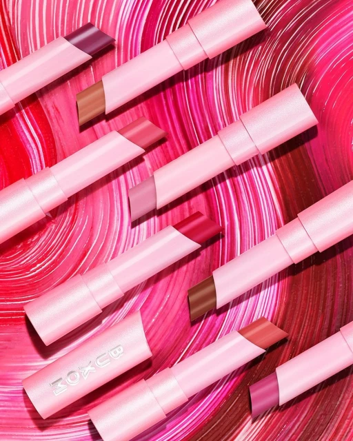Several pink lipstick tubes with varying shades of color are arranged diagonally against a red and pink swirl background.
