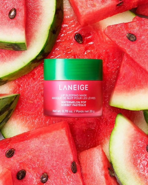 Lip sleeping mask by Laneige with watermelon pop scent surrounded by slices of watermelon. Beauty product shot on bright red surface.