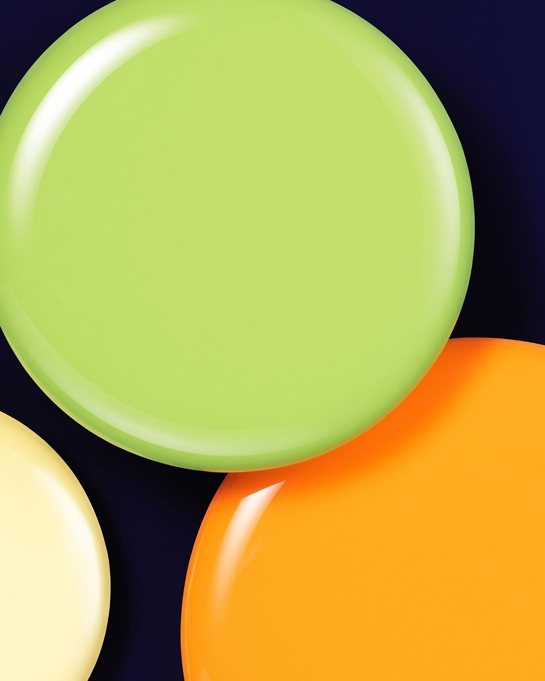 Abstract close-up of three glossy circles in lime green, orange, and pale yellow arranged against a dark blue background, studio shot.