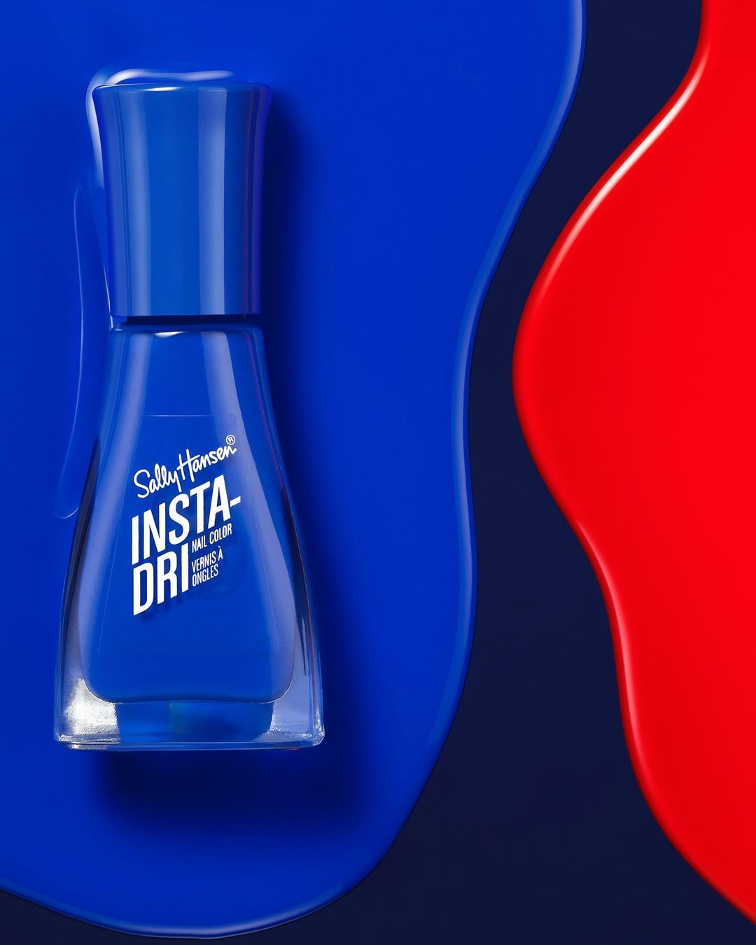 Close-up of royal blue Sally Hansen nail polish bottle with a matching royal blue nail polish puddle and contrasting red splash.