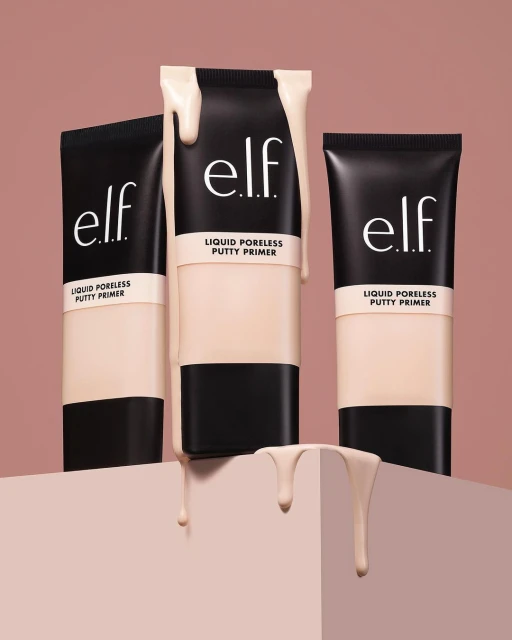 Three black tubes of e.l.f. Liquid Poreless Putty Primer are staged on a geometric stand against a light brown background, product spilling.